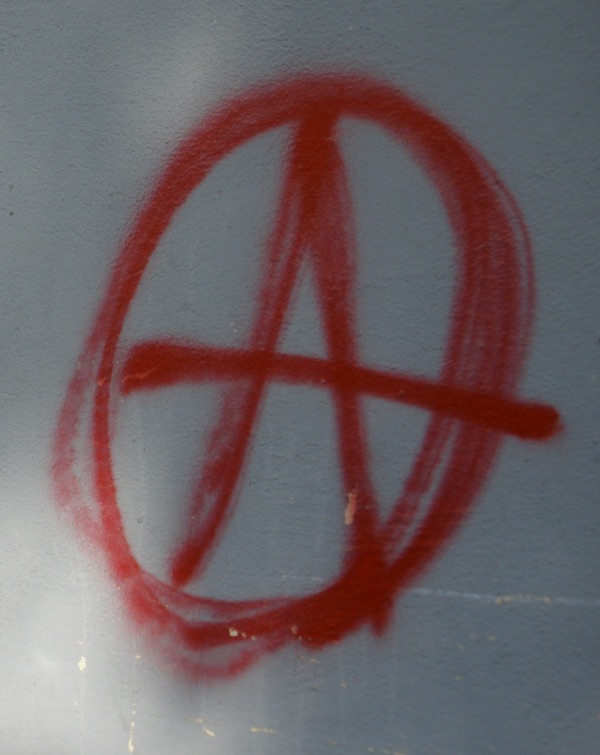 A photograph of a red, spray-painted anarchy symbol: the letter 'A' in a circle. Photographed in Athens.