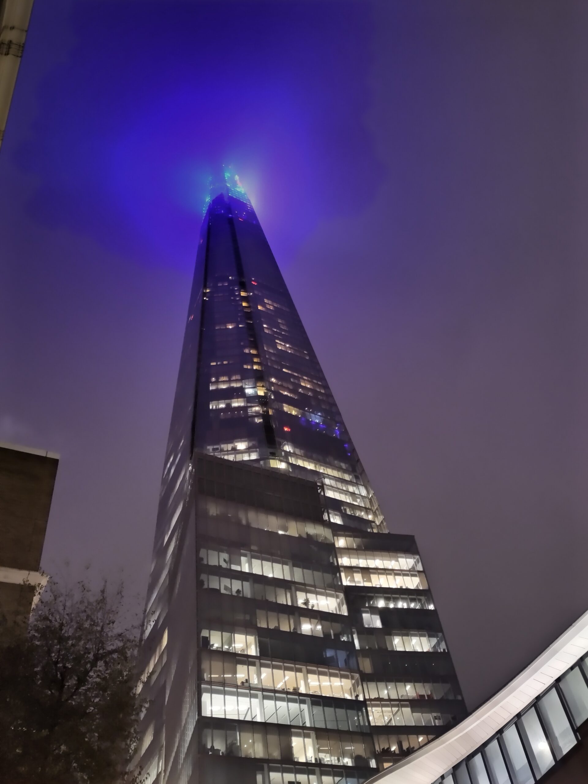 A photograph of the Shard skyscraper in London Bridge against a wintry night sky. The purple lights on the top floors spread like an apocalypse from the tower's spiky heights.