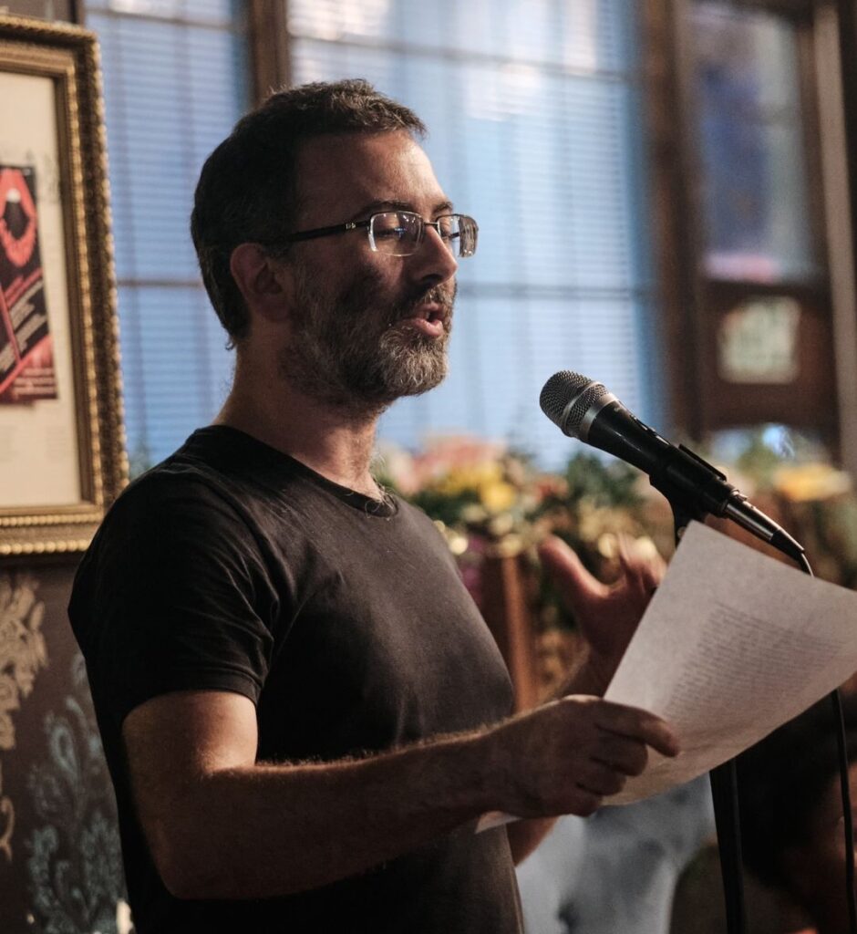 A picture of me holding a piece of paper and standing at a microphone, reading a poem.